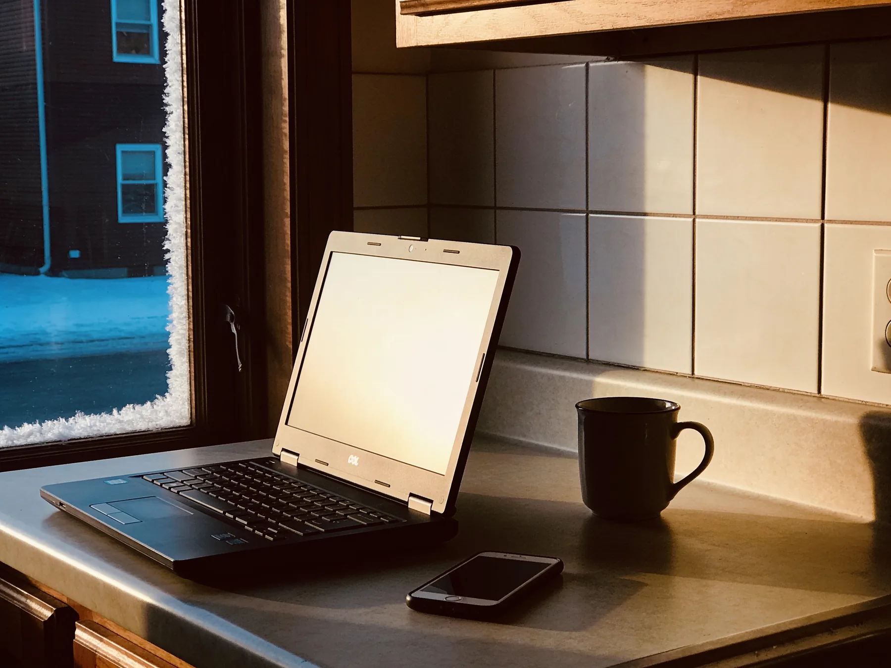 A laptop open on a kitchen counter on a dark winter morning