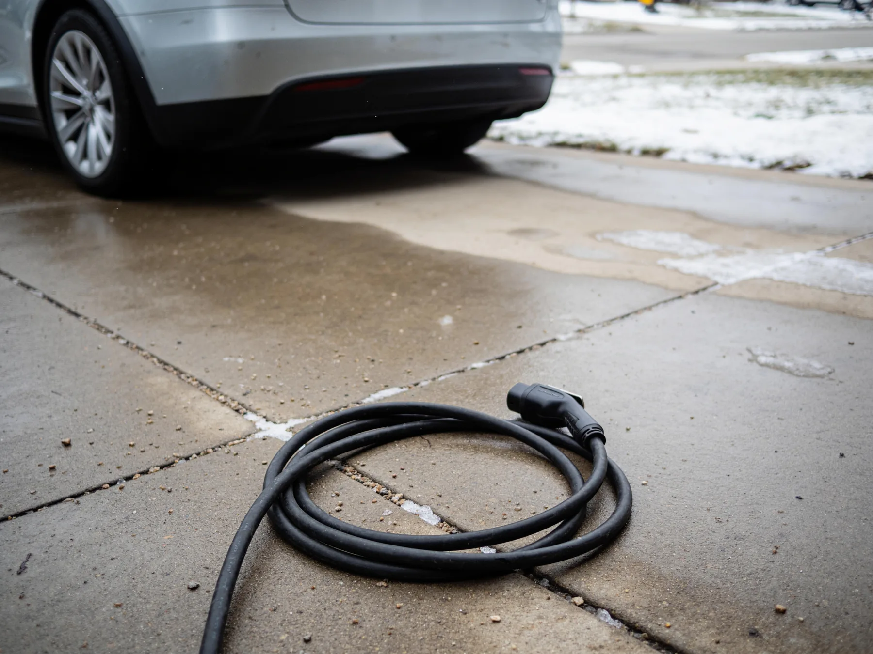 A charging cable coiled on a driveway in late winter