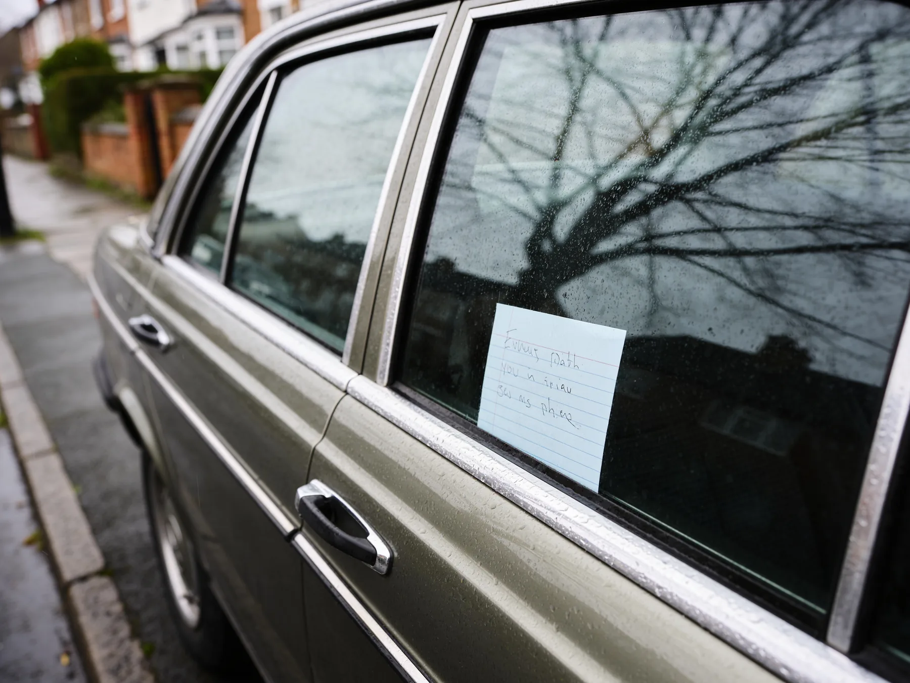 A handwritten card in a rear window on a residential street