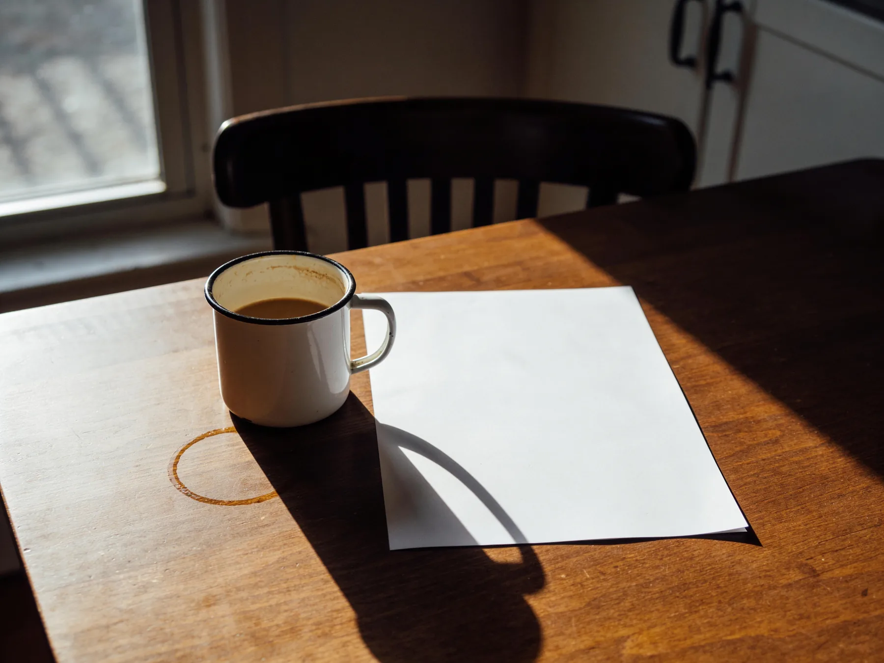 A single sheet of paper face down on a table beside a cold cup