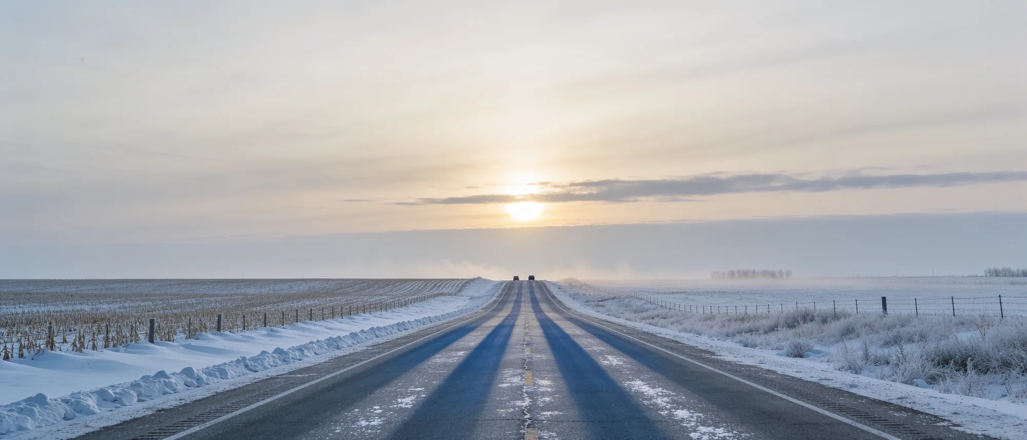 A prairie highway in winter under a low sun